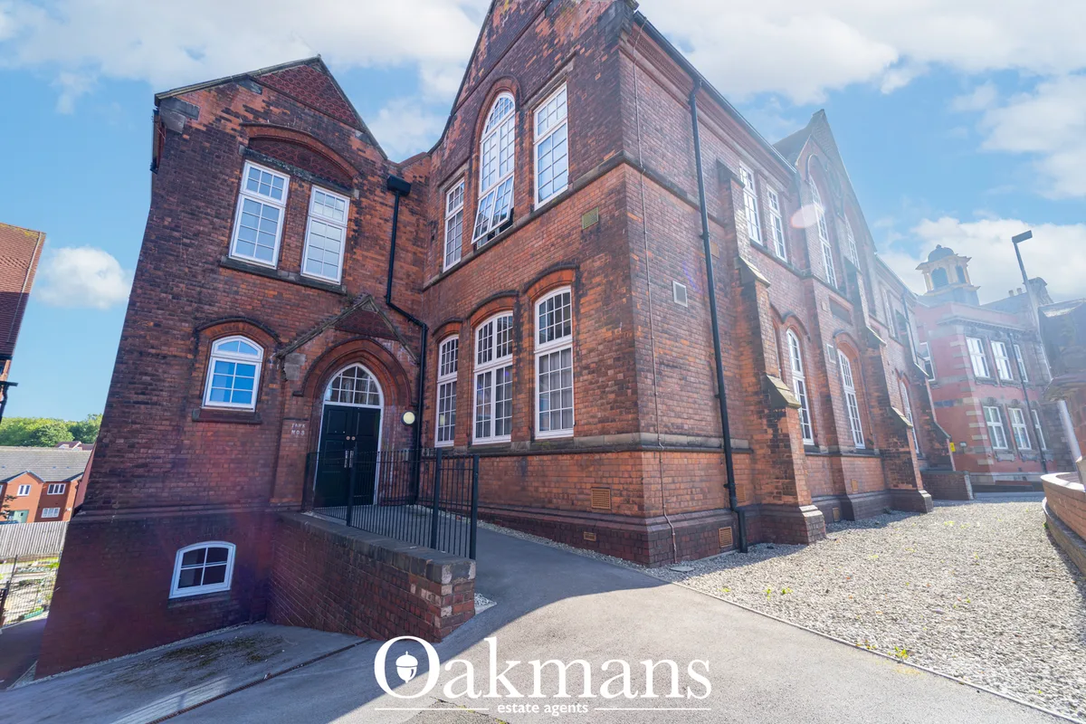 Red brick Victorian chapel building with arched windows, pitched roof, metal railings and gravel courtyard