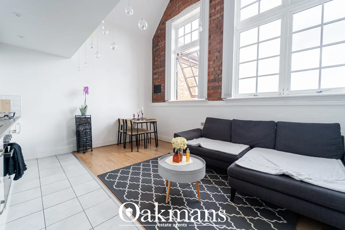 Modern loft living room with black corner sofa, grey round coffee table, large industrial windows, exposed brick, pendan