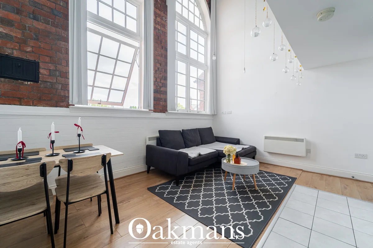 Modern living room with black sofa, round coffee table, patterned rug, large multi-pane windows, exposed brick, and pend