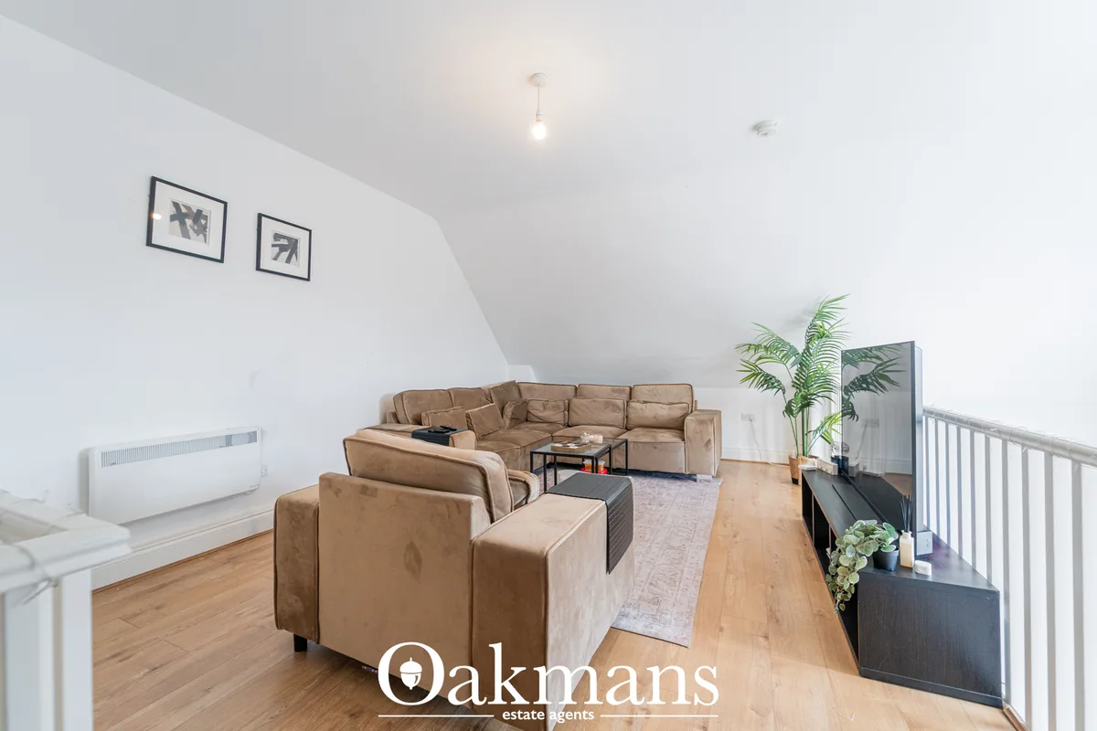 Bright open-plan living room with tan leather corner sofa, wooden flooring, pendant lighting, potted plants and white ra