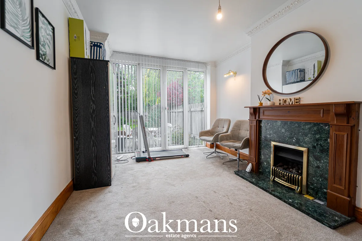 Bright living room with fireplace, round mirror, two tan chairs, glass patio doors overlooking garden, pendant lighting