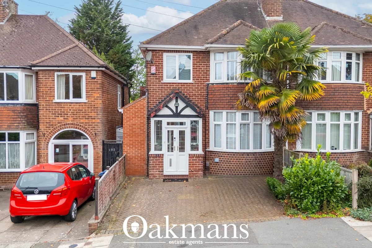 Semi-detached brick house with red-tiled roof, white bay windows, palm tree, driveway with red car parked outside, and w