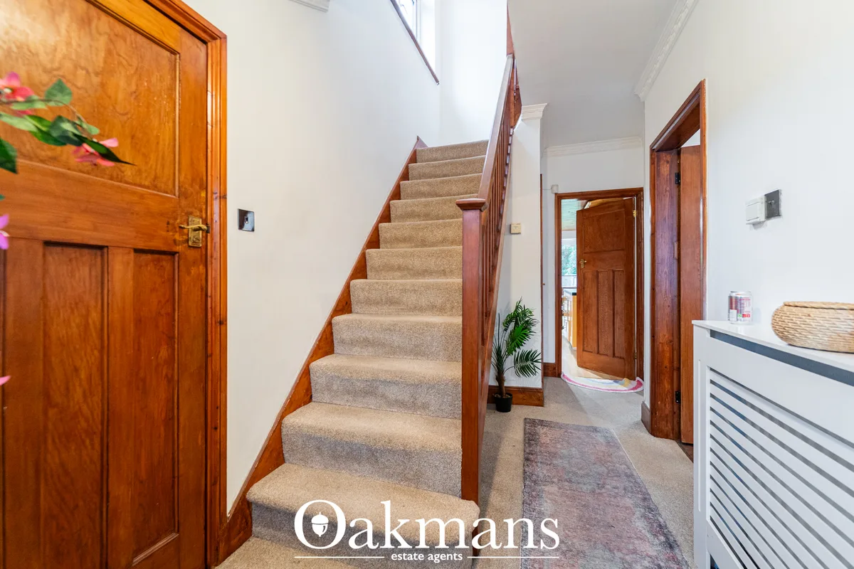 Bright entrance hallway with wooden doors, carpet staircase with wood railings, white walls and potted plants