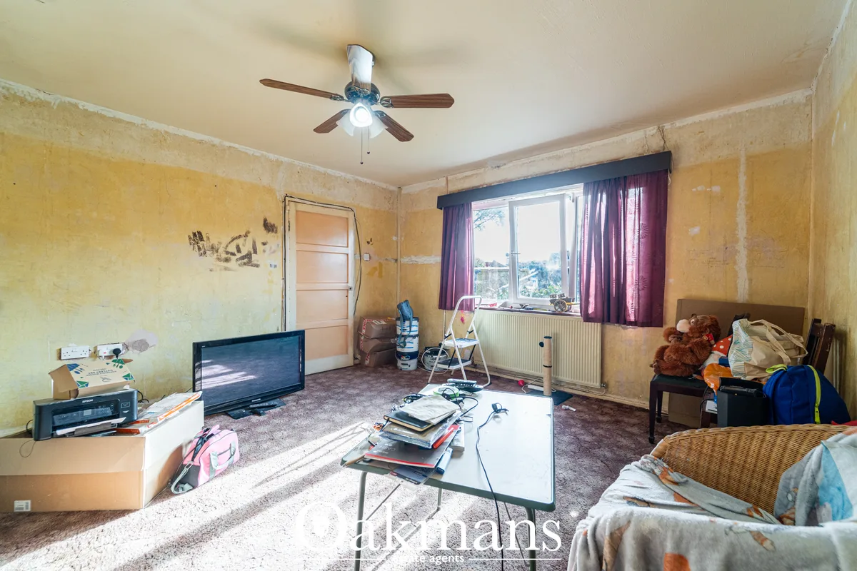Spacious living room with yellow walls, ceiling fan, TV on stand, settee, storage boxes, large window with purple curtai