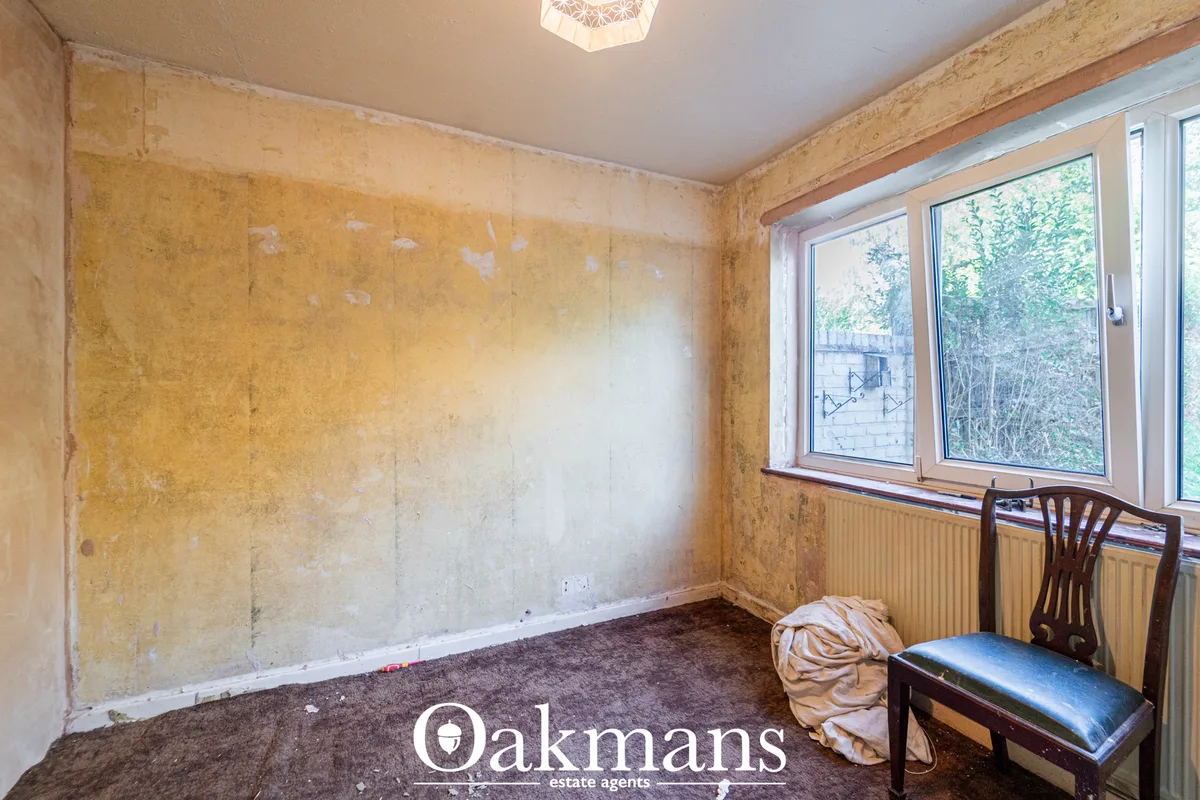 Unfurnished study room with stained walls, wooden beam, radiator, windows overlooking garden, and single chair