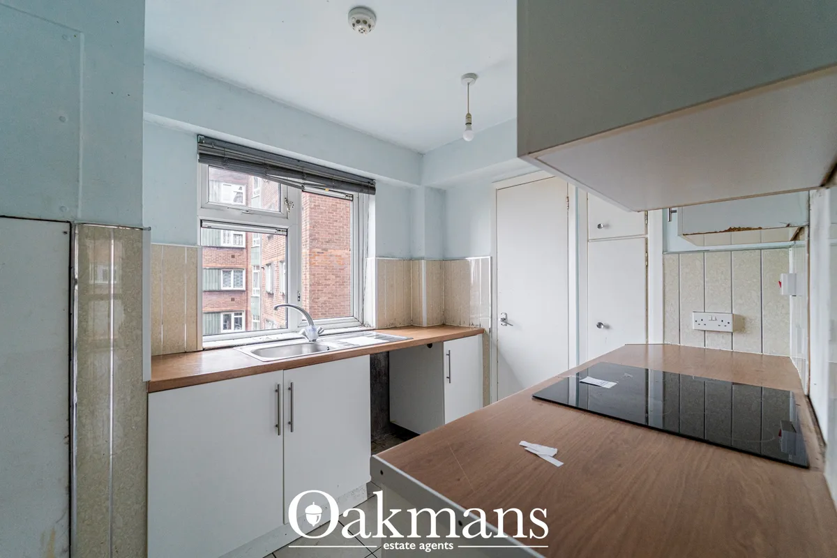 Modern kitchen with white units, wooden worktops, sink under window overlooking brick building, tiled splashback