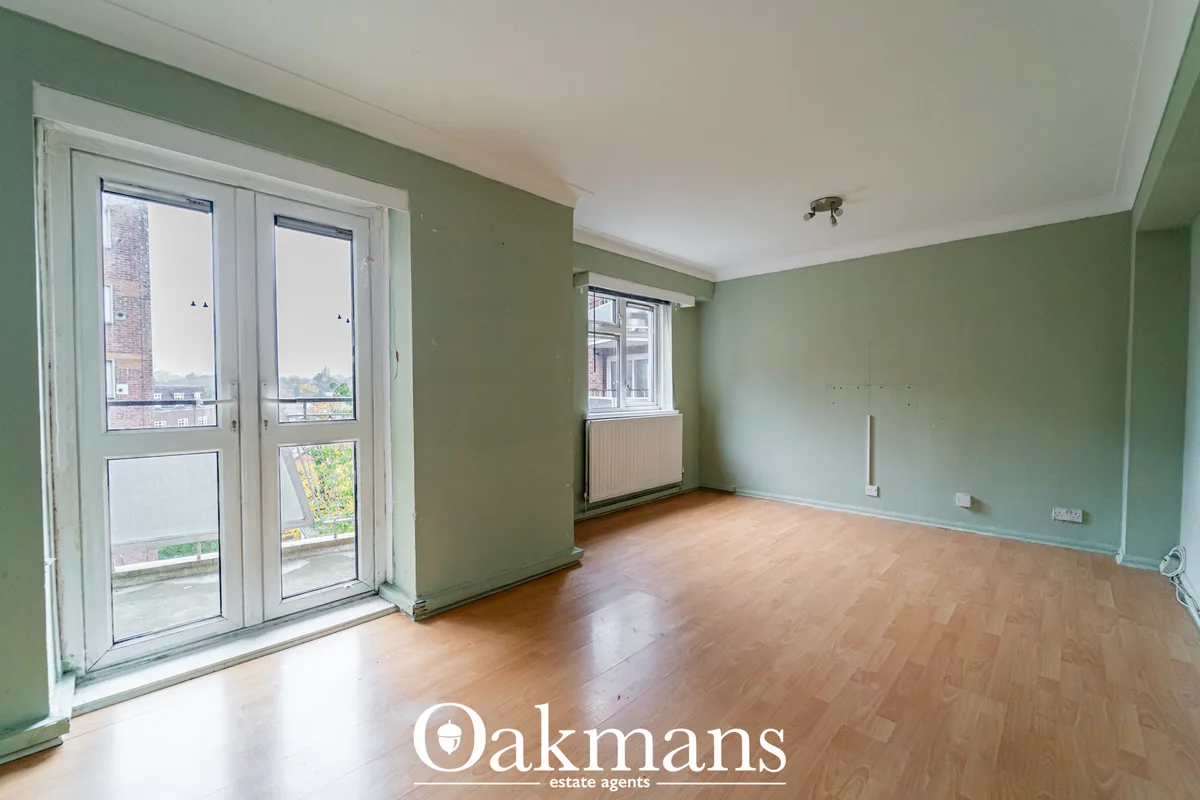 Bright living room with sage green walls, wooden flooring, patio doors overlooking balcony, radiator and window with str
