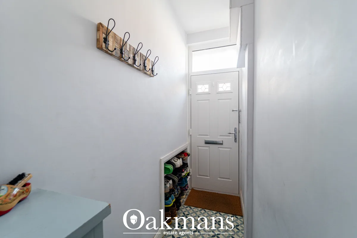 Bright entrance hallway with white walls, wooden coat rack, white panelled front door with transom window, shoe storage 