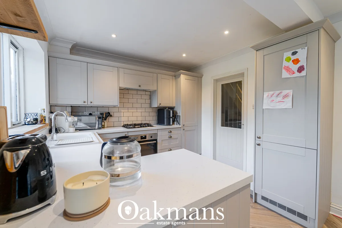 Modern white fitted kitchen with subway tile splashback, gas hob, white worktops, island seating, and integrated applian
