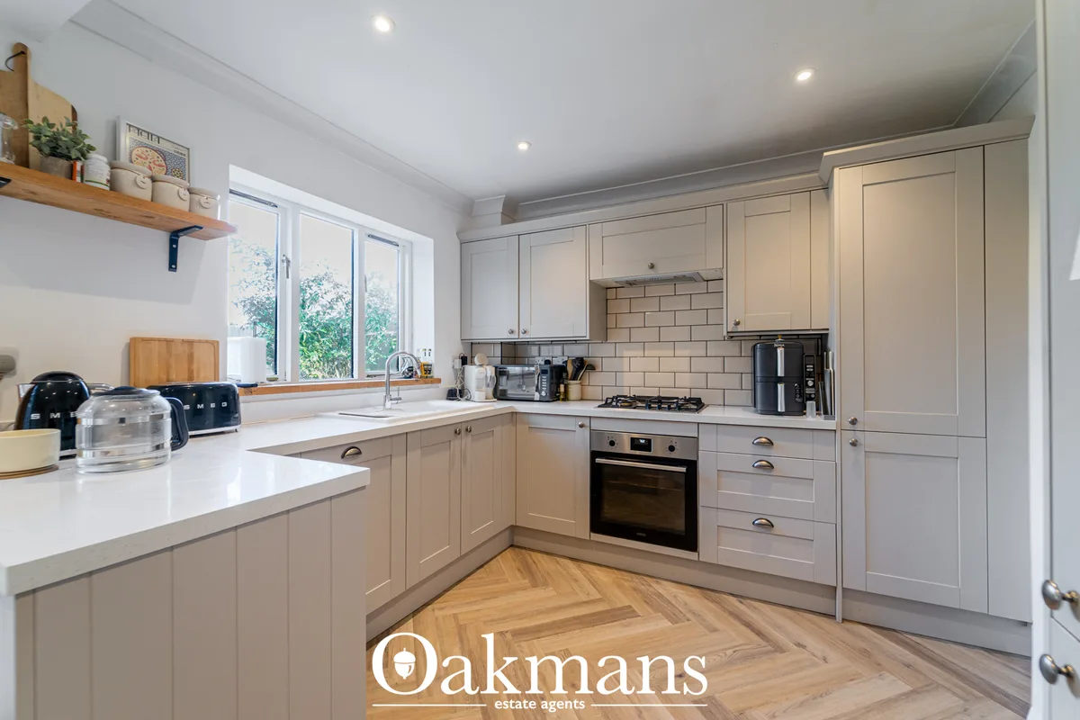 Modern fitted kitchen with cream cabinetry, white worktops, subway tile splashback, gas hob, built-in oven and herringbo