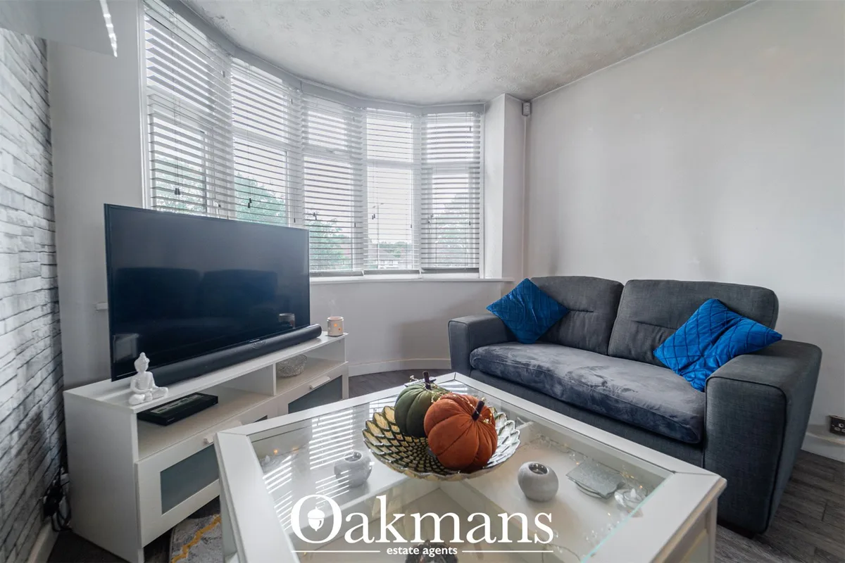 Modern living room with grey sofa, blue cushions, wall-mounted TV, white media unit, glass coffee table with decorative 