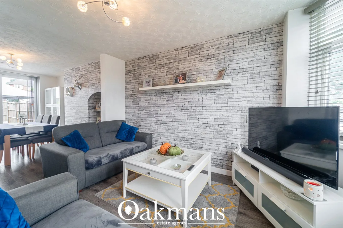 Open-plan living room with grey sofa, white coffee table, flat-screen TV on stand, and decorative brick feature wall wit