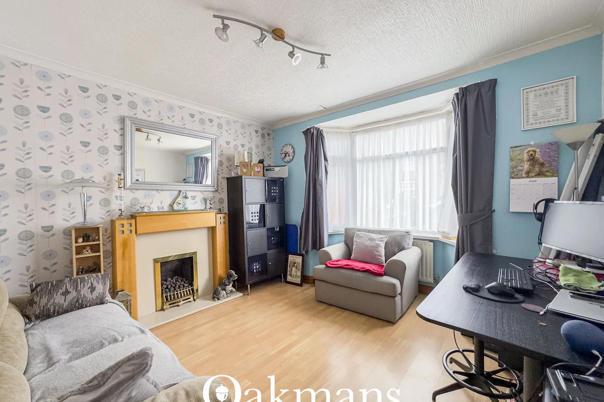 Bright living room with fireplace, beige sofa, armchair, desk, large windows with grey curtains, patterned wallpaper, wo