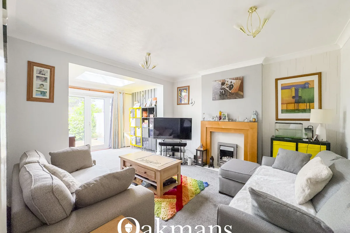 Bright living room with grey upholstered sofas, wooden fireplace, TV, striped armchair, wooden coffee table and colourfu