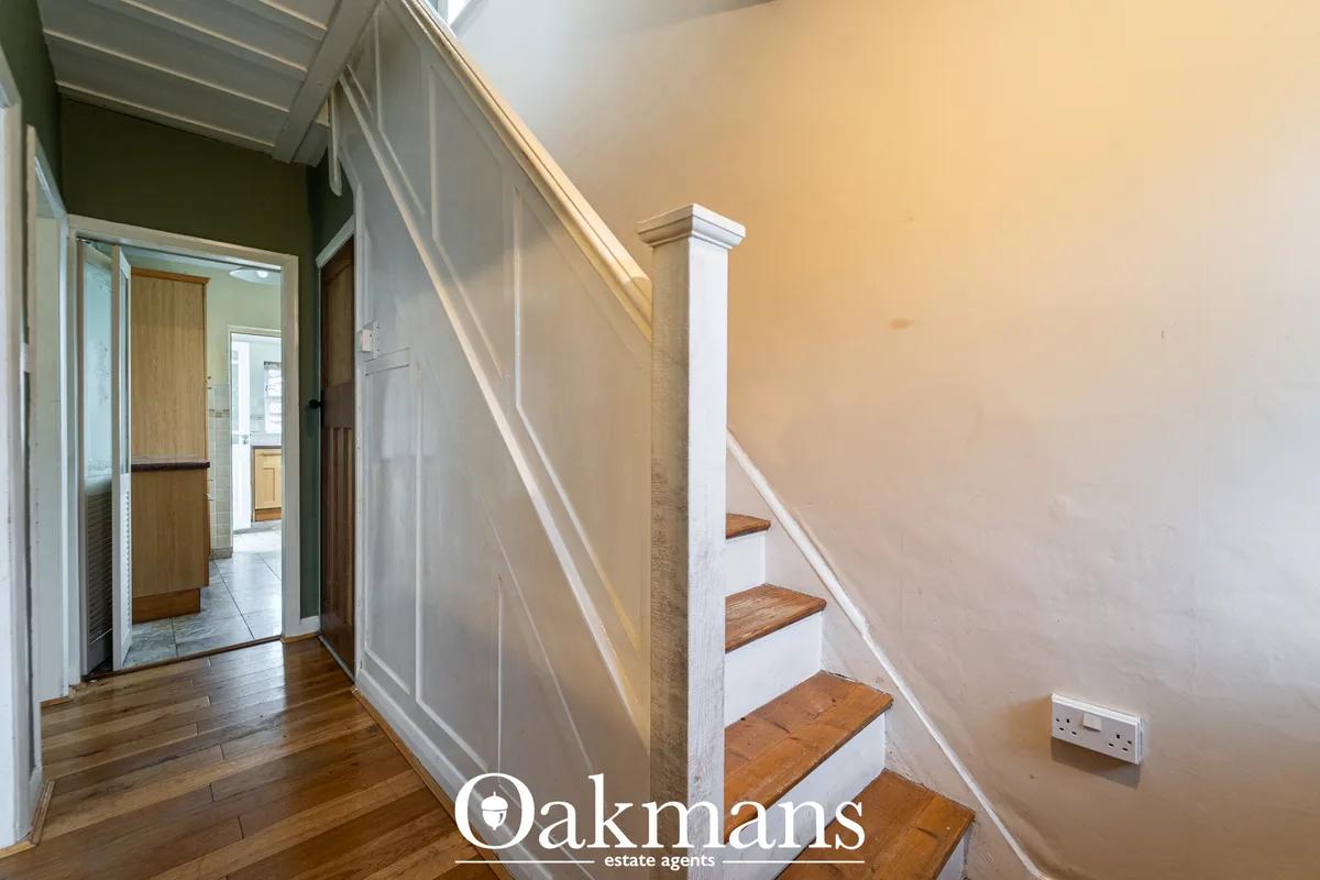Bright hallway with wooden stairs, white banister and newel post, wooden flooring, cream walls and recessed lighting