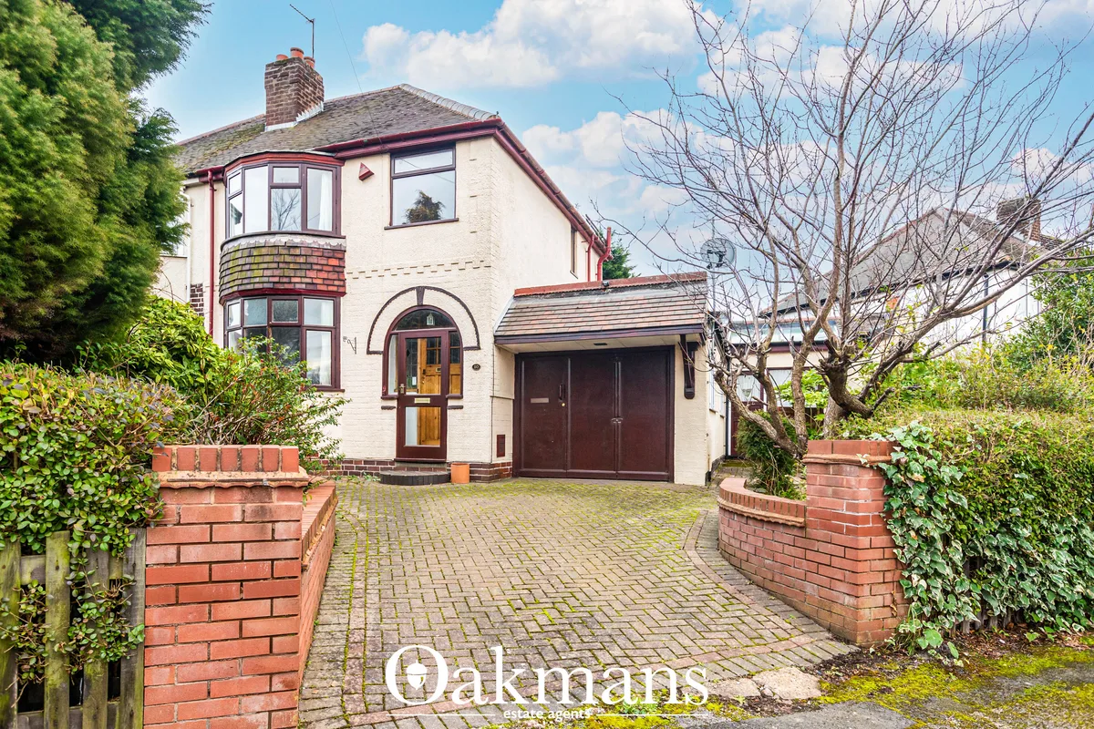Cream and red-brick semi-detached house with bay window, arched entrance door, attached garage, driveway and mature hedg
