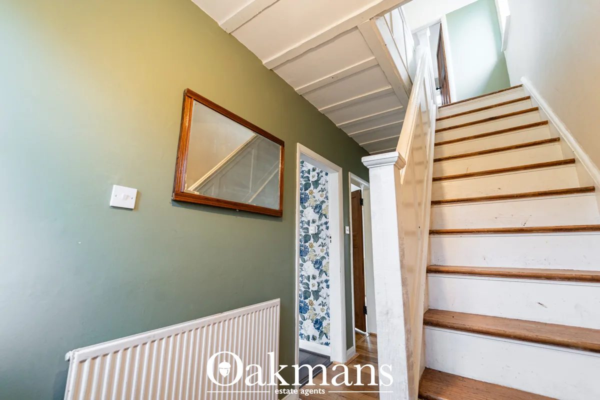 Green-painted hallway with wooden staircase, radiator, framed mirror, and white ceiling with exposed beams