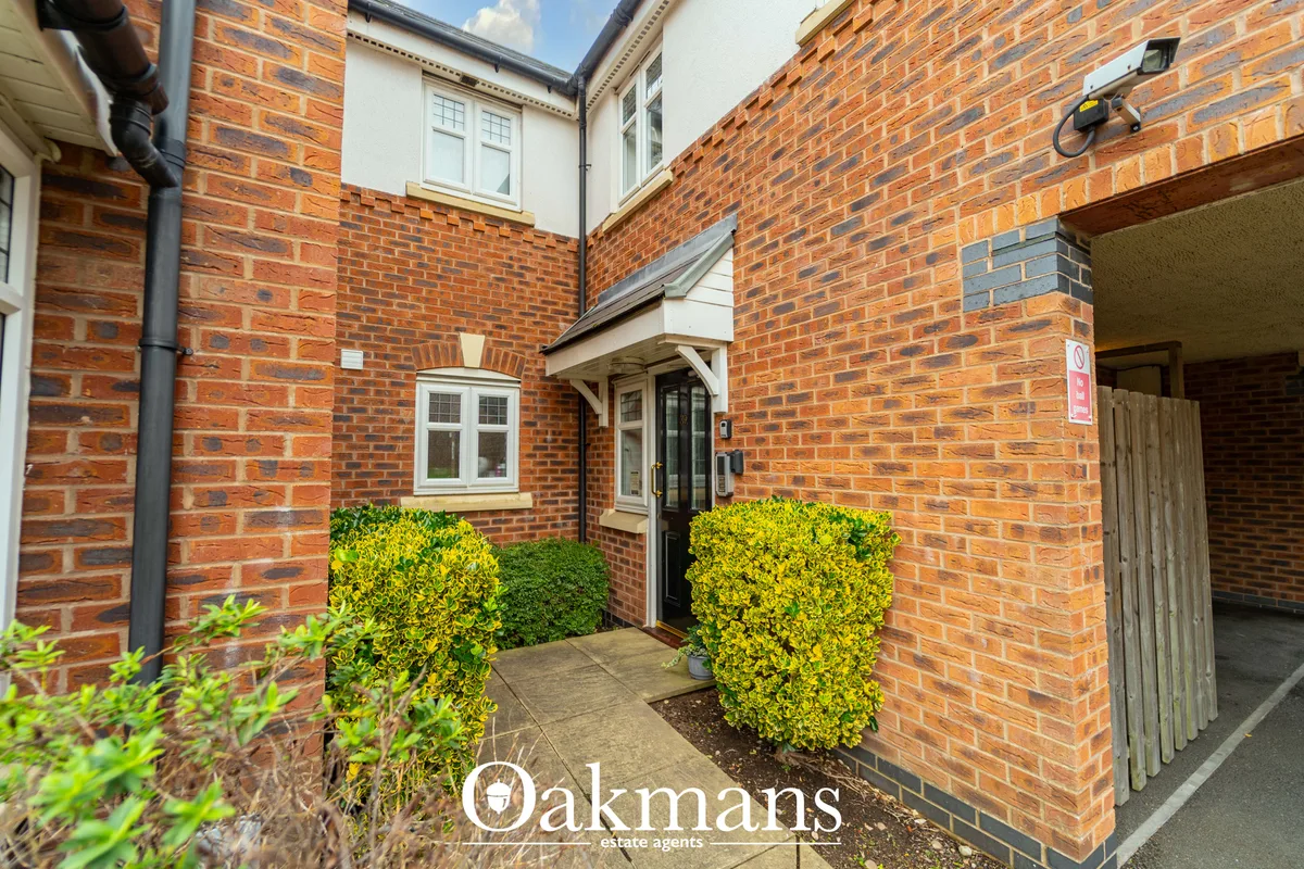 Brick courtyard entrance with double doors, flanked by manicured hedges, leading to terraced property