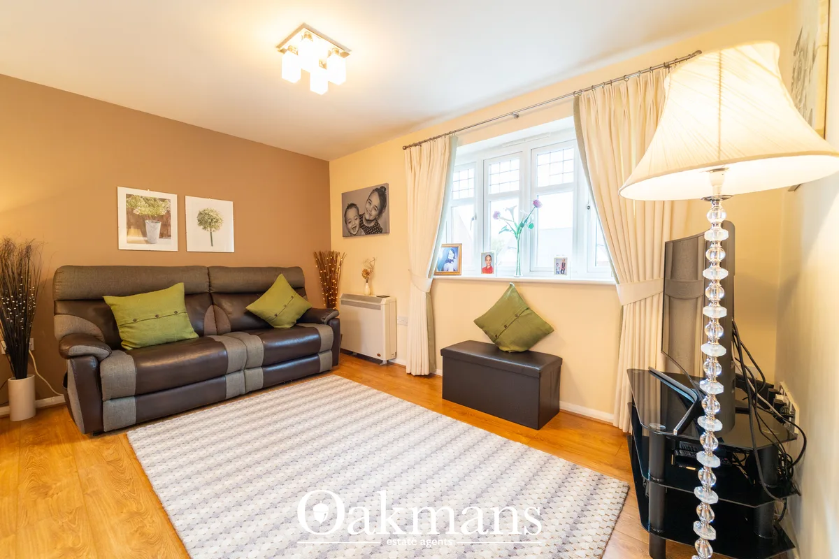 Warm living room with brown leather reclining sofa, large bay window with cream curtains, wooden flooring, and contempor