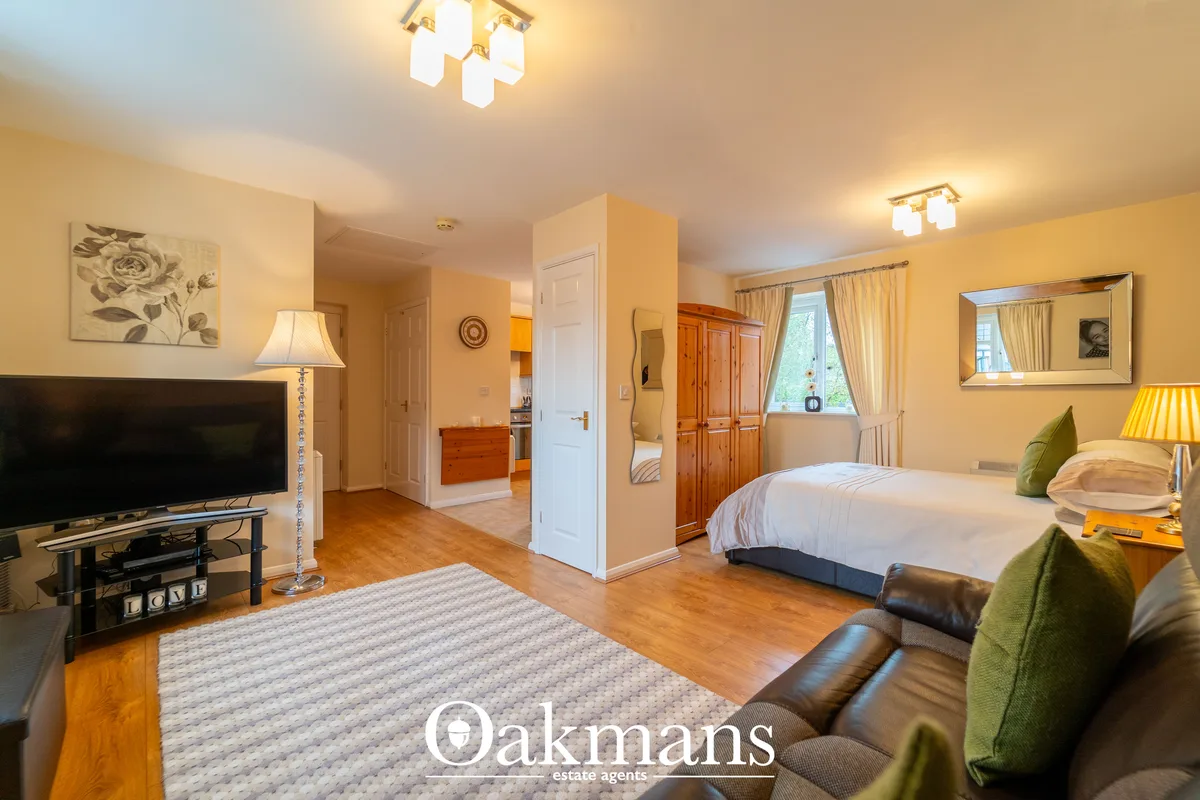 Spacious bedroom with double bed, wooden wardrobes, mirror, cream walls, wooden flooring, TV, and windows with curtains 