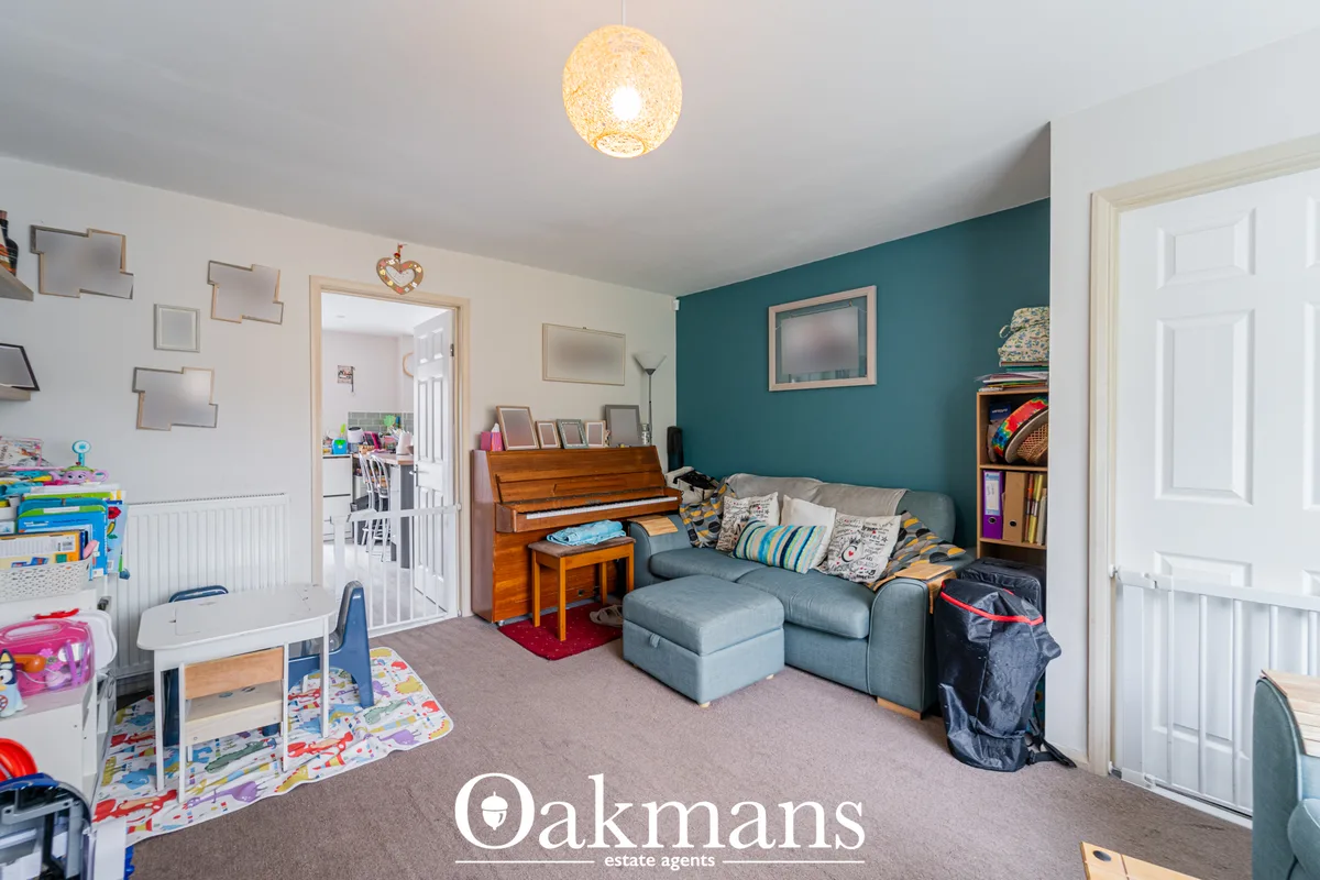 Multi-purpose living room with teal accent wall, grey corner sofa, wooden piano, framed artwork and storage shelving, br