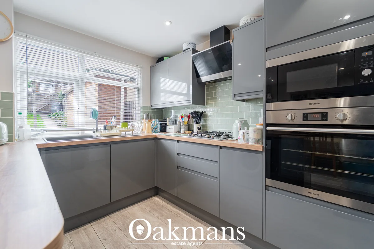 Modern fitted kitchen with grey cabinetry, wooden worktops, sage green subway tile splashback, stainless steel appliance