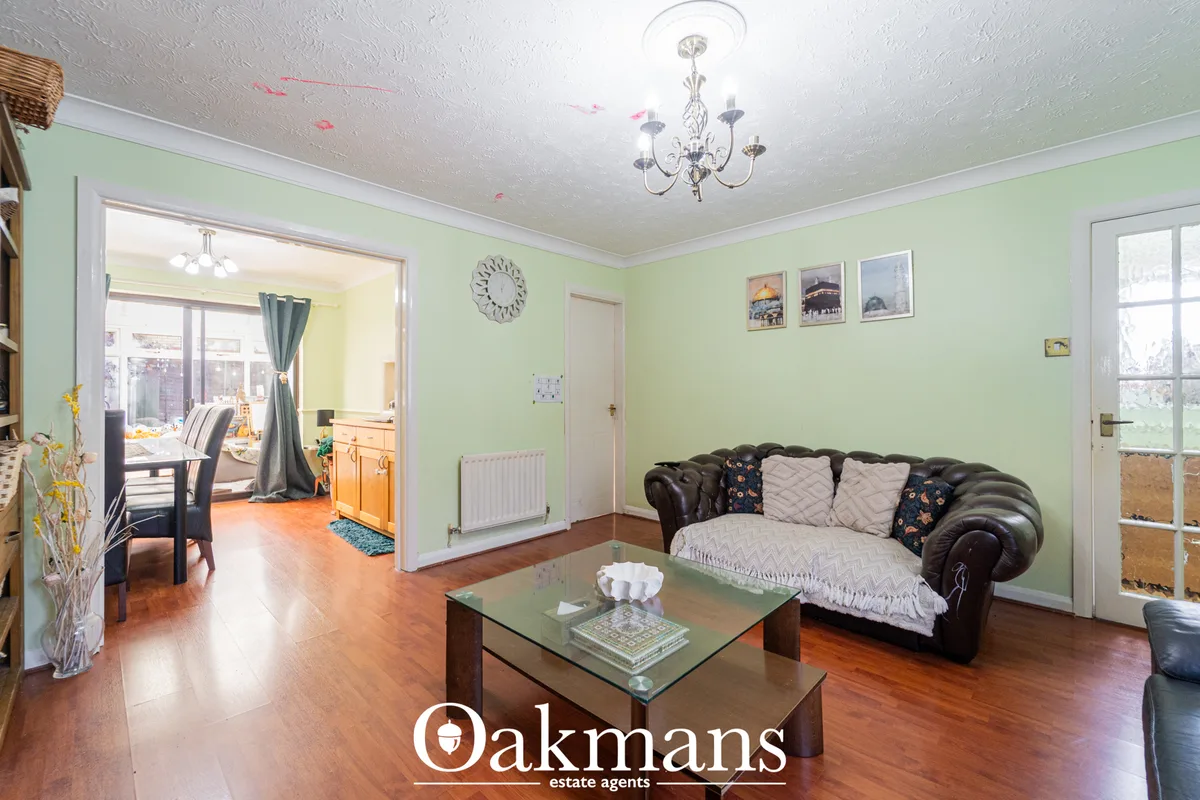 Spacious living room with pale green walls, dark leather Chesterfield sofa, glass coffee table, wooden flooring and acce