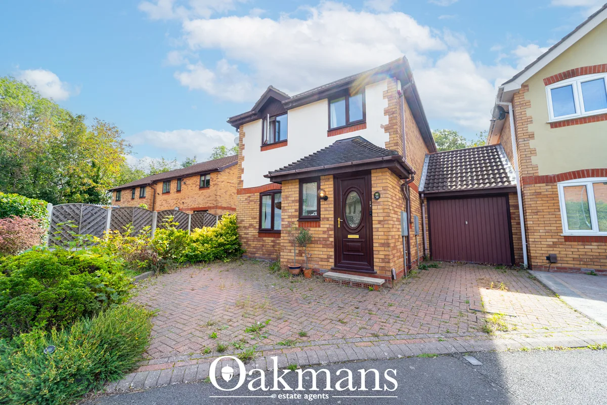 Brick-built detached house with white render upper storey, dark red door, garage, paved driveway and mature gardens