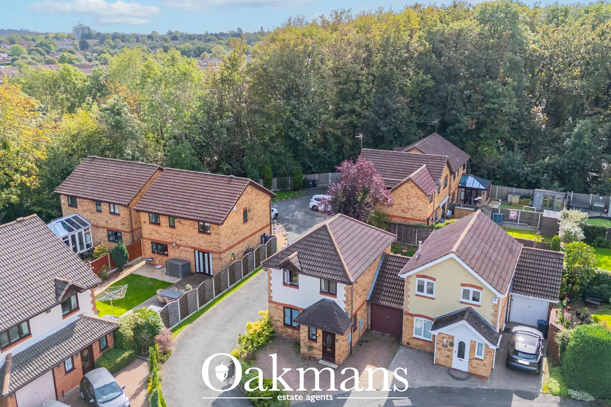 Aerial drone photograph of residential properties with brick construction, dark tile roofs, driveways, manicured gardens