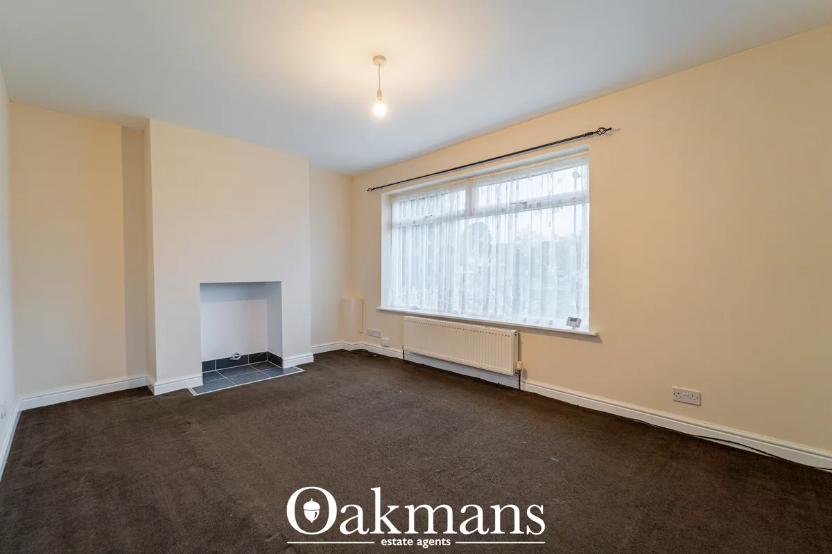 Spacious living room with cream walls, dark carpet, fireplace with black tiles, large window with sheer curtains and rad