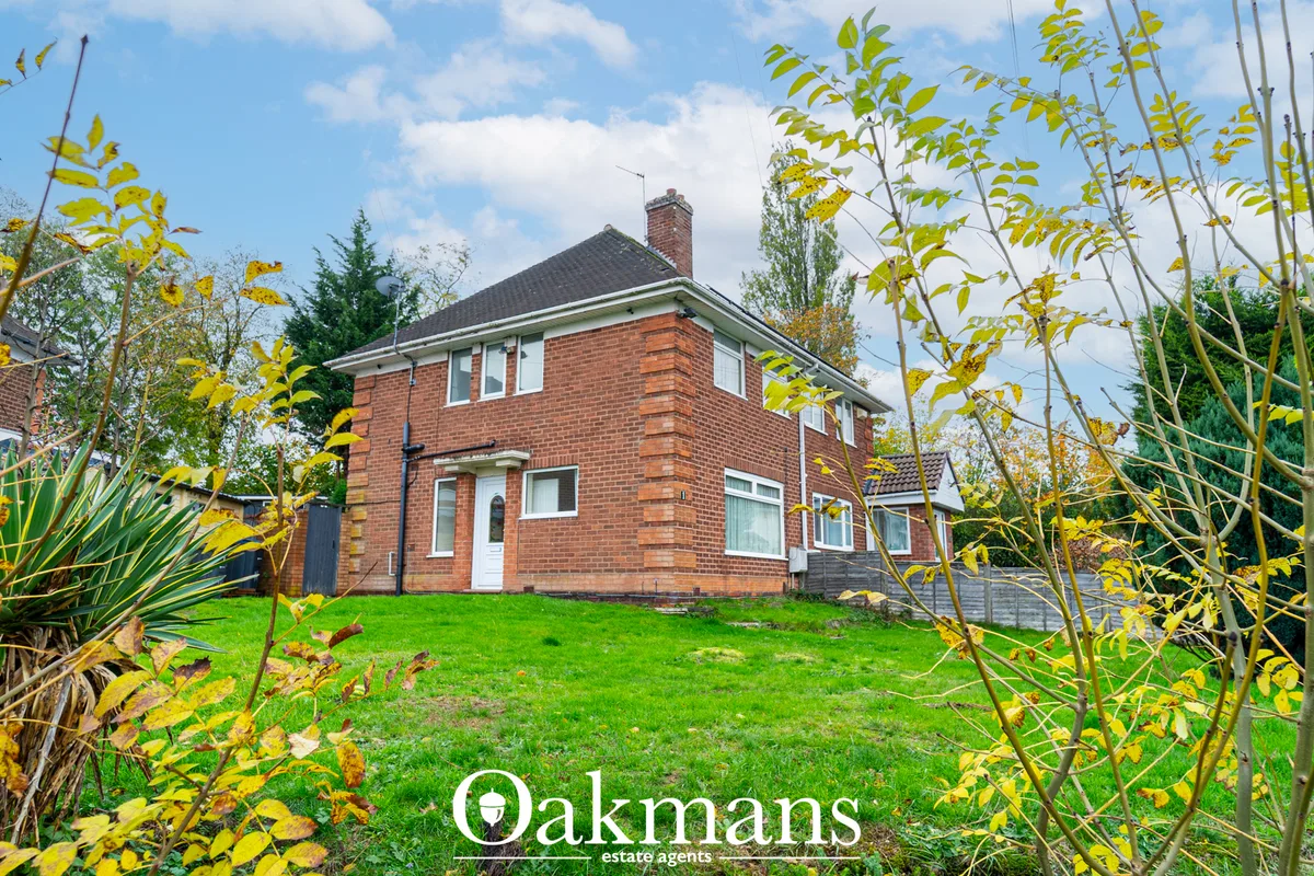 Red brick two-storey detached house with white trim, chimney and pitched roof, viewed across lawn with autumn foliage fr