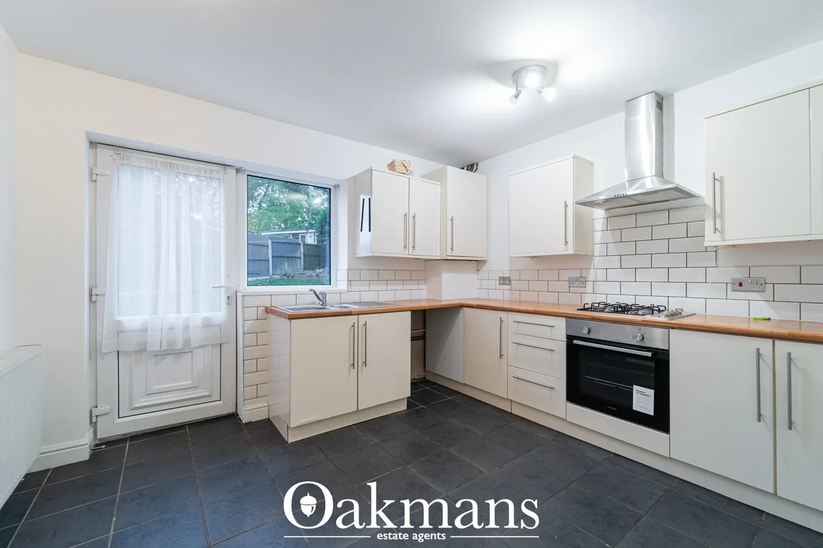 Modern fitted kitchen with cream units, wooden worktops, white subway tile splashback, built-in black oven, gas hob and 