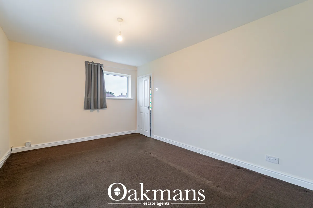 Spacious bedroom with cream and white walls, dark carpet flooring, window with grey curtains, white door, and pendant ce