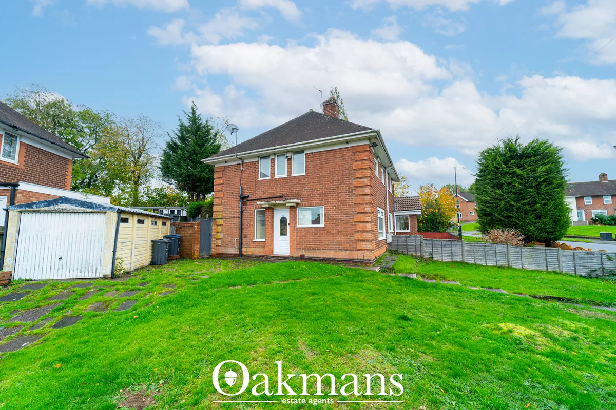 Red brick detached house with white door and windows, large front lawn, garages and hedged boundaries on suburban street