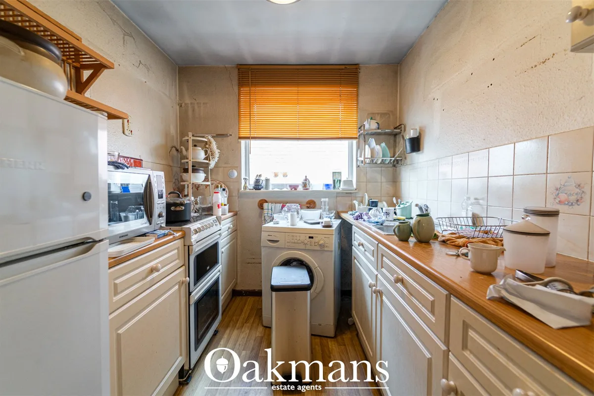 Galley kitchen with cream and white fitted units, wooden worktops, integrated appliances, washing machine, window with o