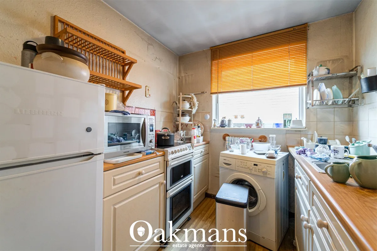 Galley kitchen with cream cabinetry, integrated appliances, wooden worktops, washing machine, window with wooden blinds 