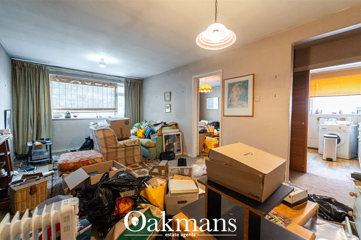 Cluttered living room with cardboard boxes, black bags, furniture and personal items throughout the space