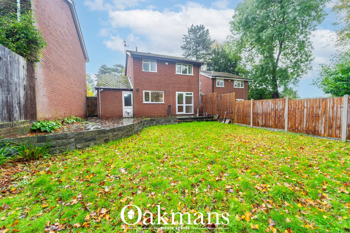 Brick-built two-storey house with rear garden lawn, fallen autumn leaves, wooden fence, stone boundary wall and mature t