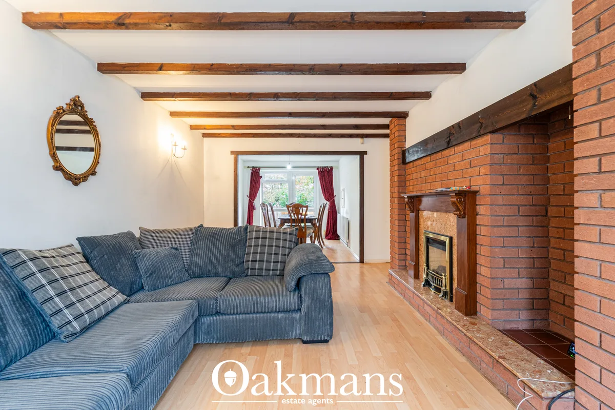 Spacious living room with exposed wooden beams, blue striped sofa, brick fireplace with wooden mantelpiece, and doorway 