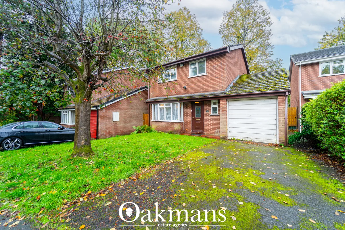 Red brick two-storey detached house with white garage door, driveway, mature trees and green lawn with parked car