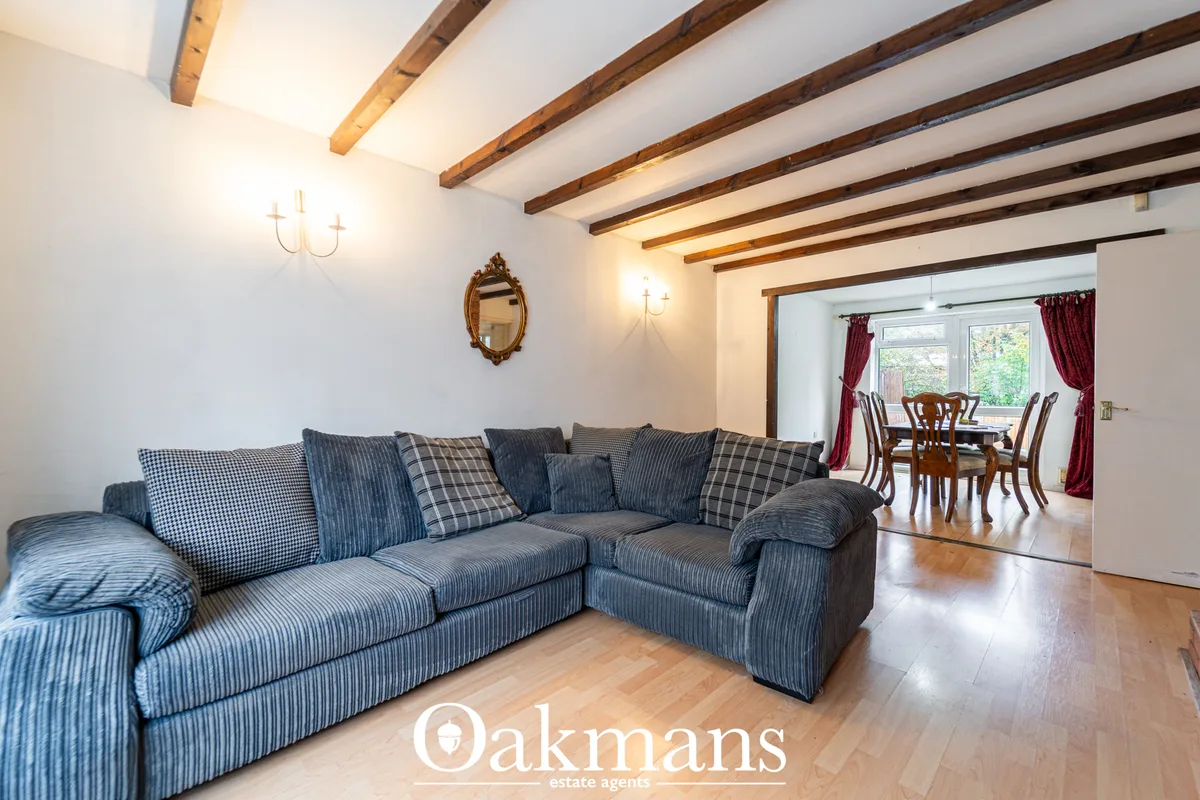 Open-plan living room with blue striped corner sofa, exposed wooden beams, wall sconces, ornate mirror, and doorway to d