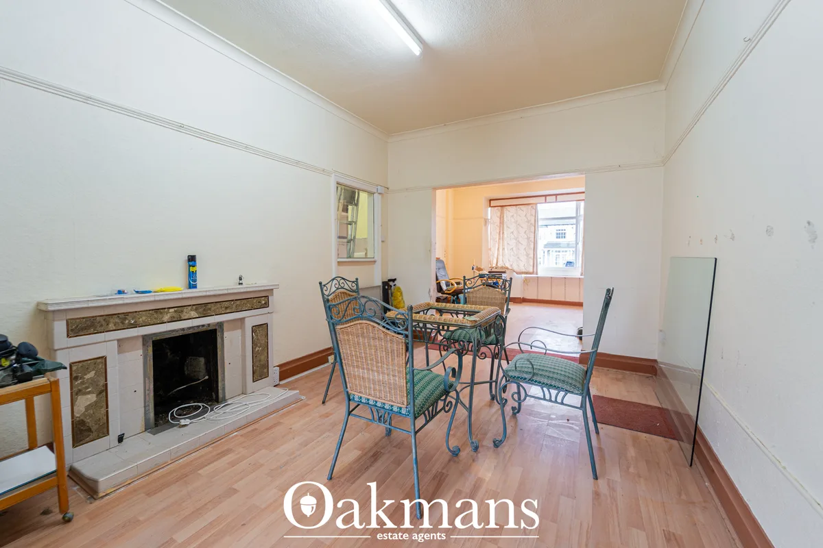 Spacious living room with decorative fireplace, wooden flooring, metal framed chairs around dining table, and access to 