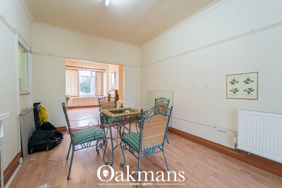 Spacious dining room with wooden flooring, cream walls, metal-frame dining chairs with woven seats, and large window ove