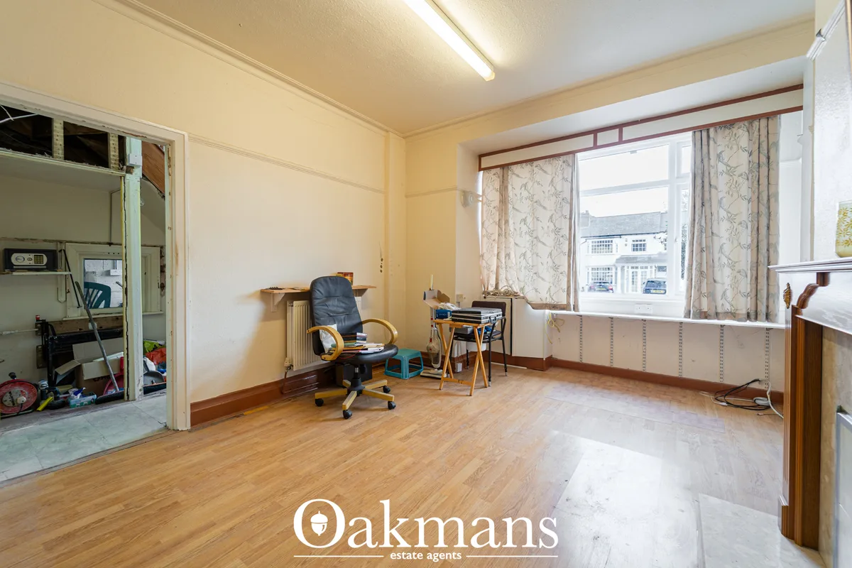 Spacious bedroom with wooden flooring, large window with patterned curtains, office chair, desk, radiator and storage ar
