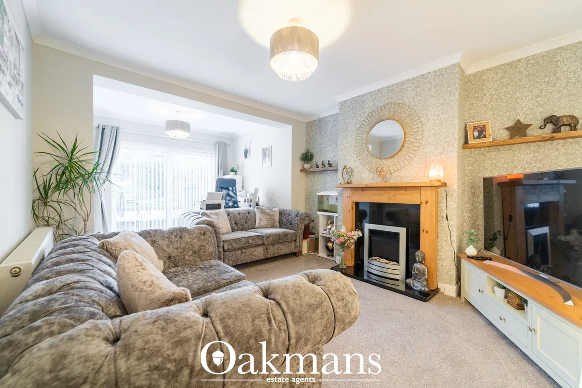 Spacious living room with patterned upholstered seating, wooden fireplace surround, decorative shelving, patterned wallp