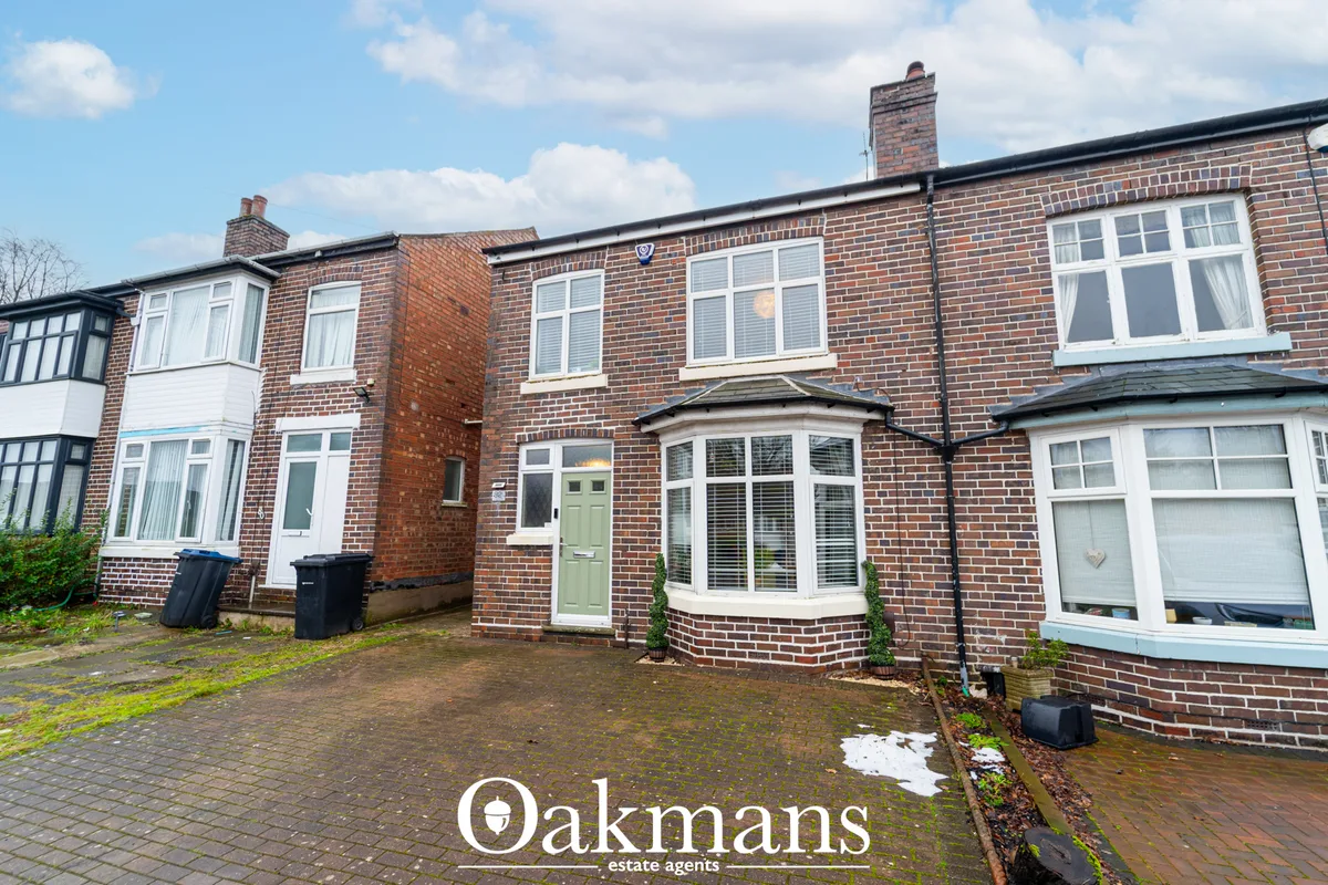 Red brick terraced houses with white window frames, green front door, pitched roofs with chimneys, driveway and hedge bo