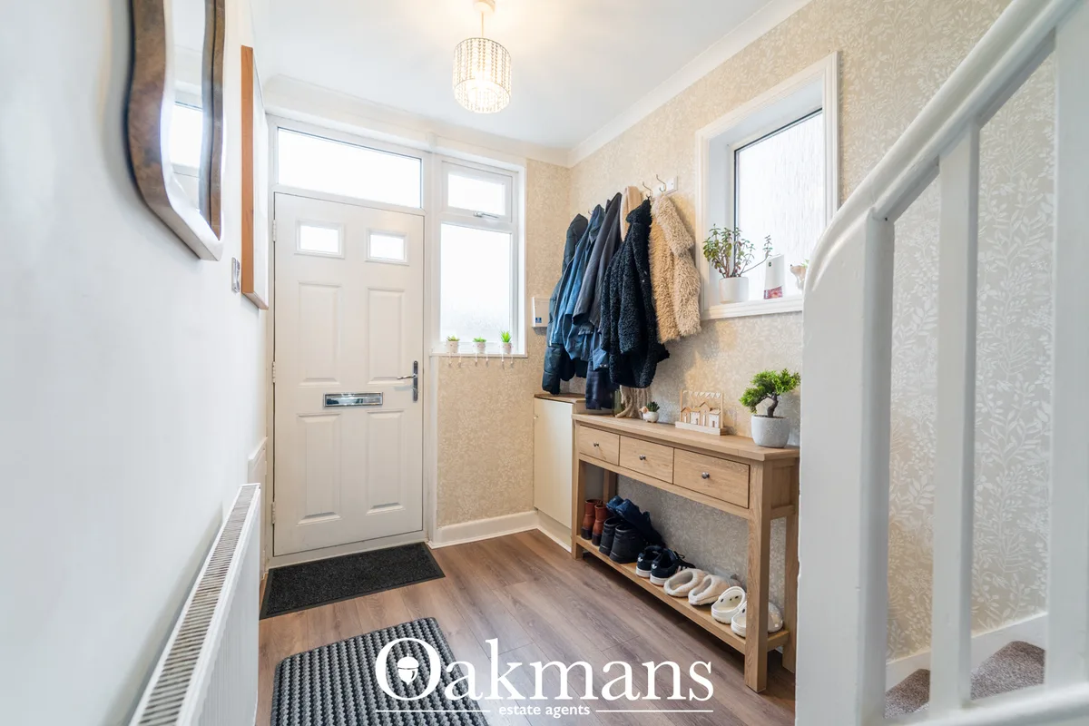 Bright entrance hallway with cream front door, wooden console table, coat hooks, potted plants, wooden flooring and neut