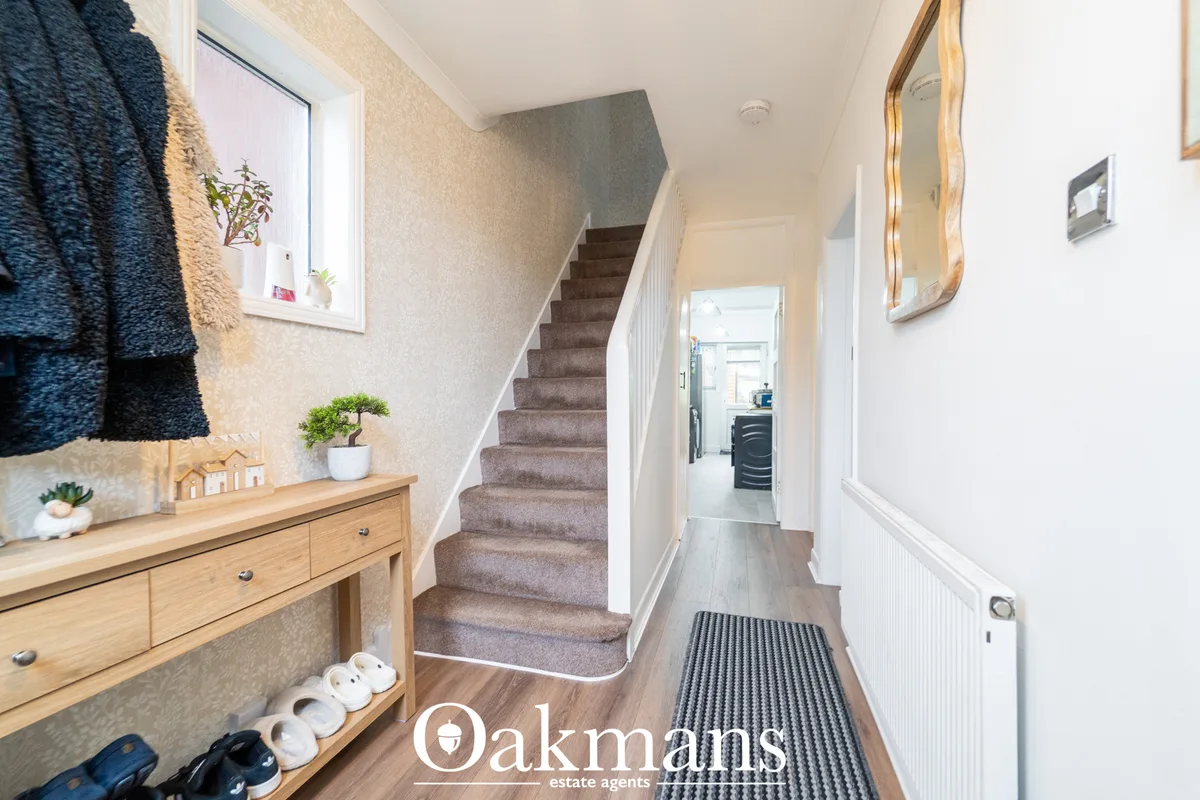 Bright hallway with wooden staircase, cream walls, wooden console table, mirror, and dark runner mat leading to kitchen