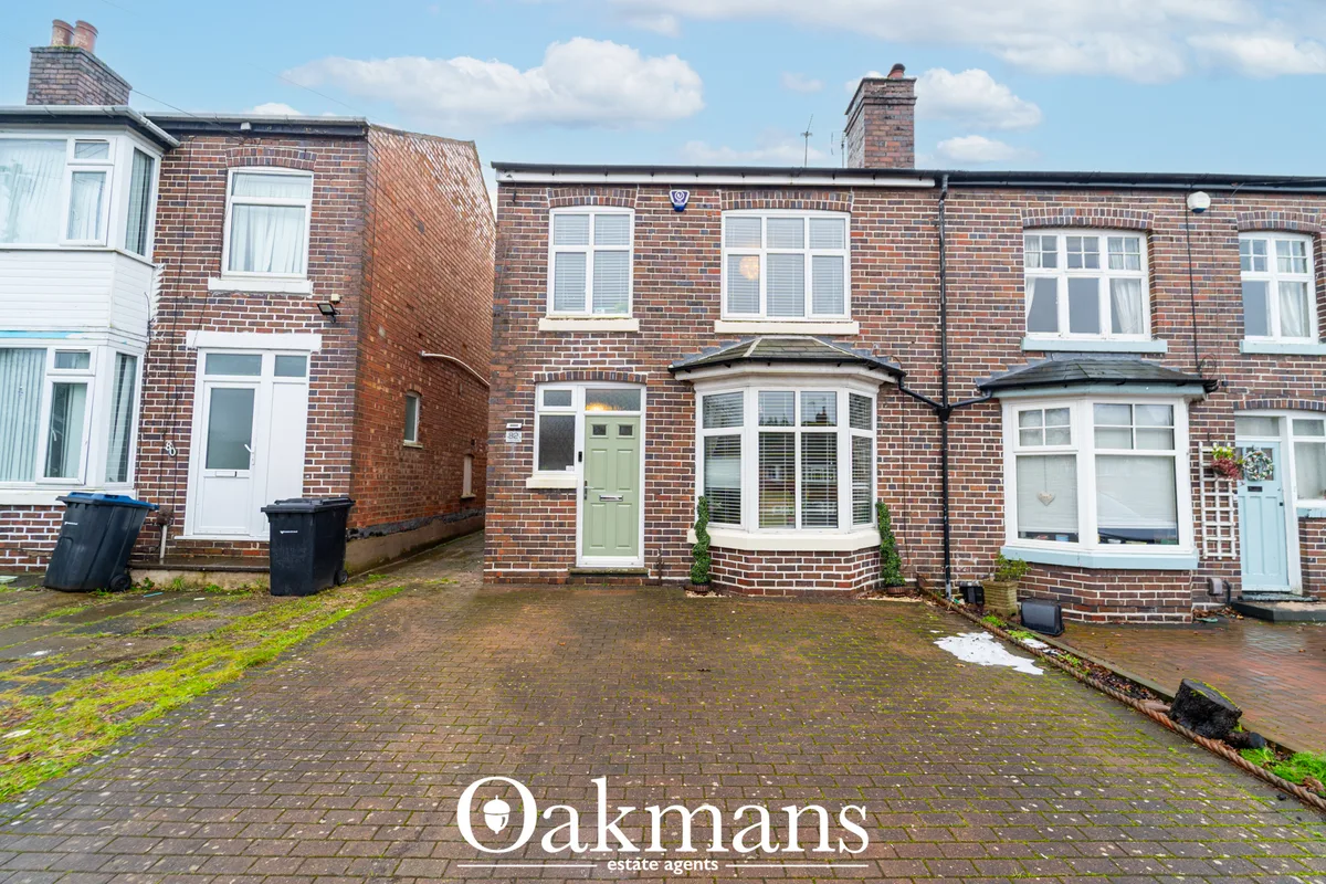 Brick terraced houses with green doors and bay windows, brick driveways and blue bins, overcast sky