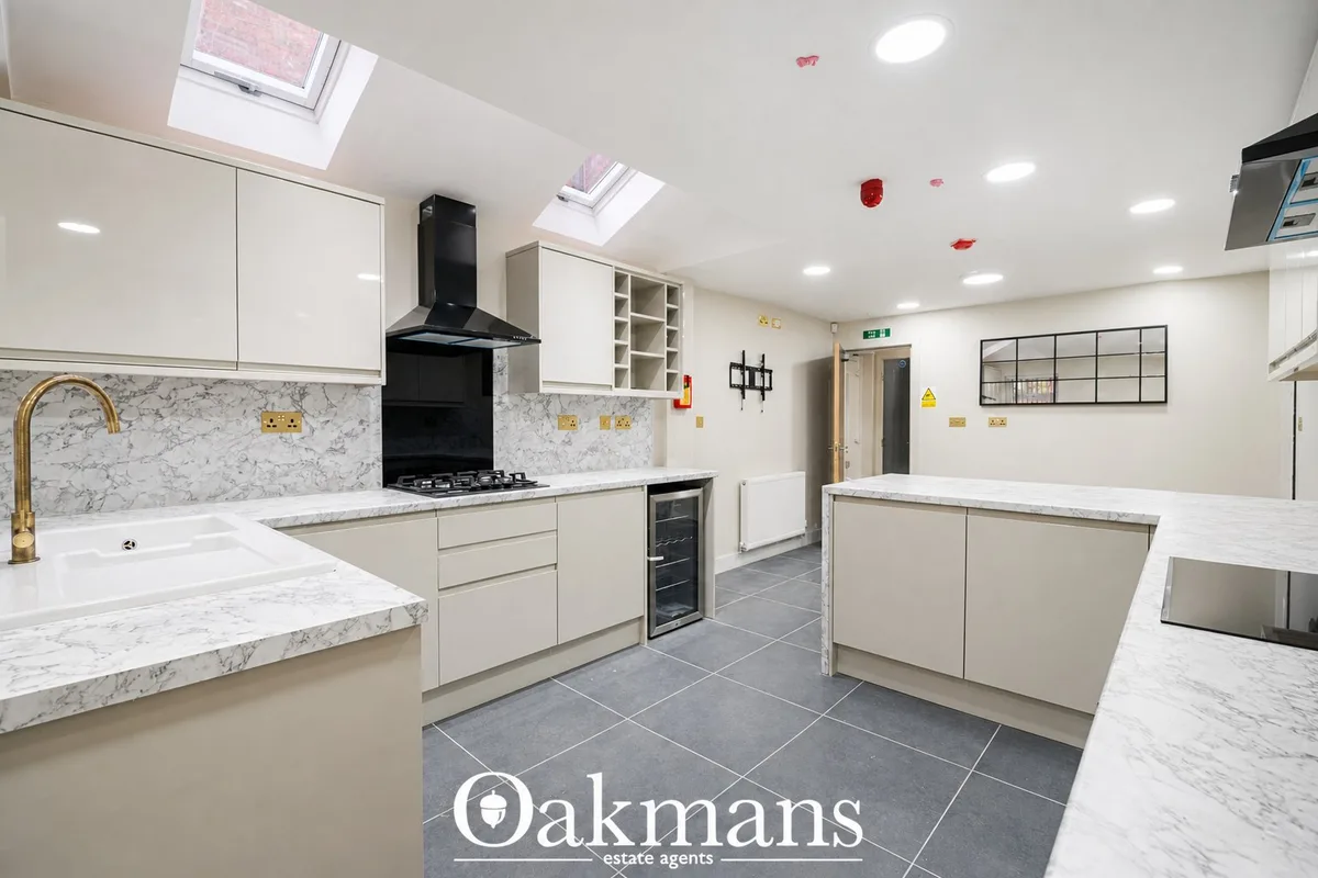 Modern fitted kitchen with white units, marble worktops, black gas range cooker, skylight windows and breakfast bar seat
